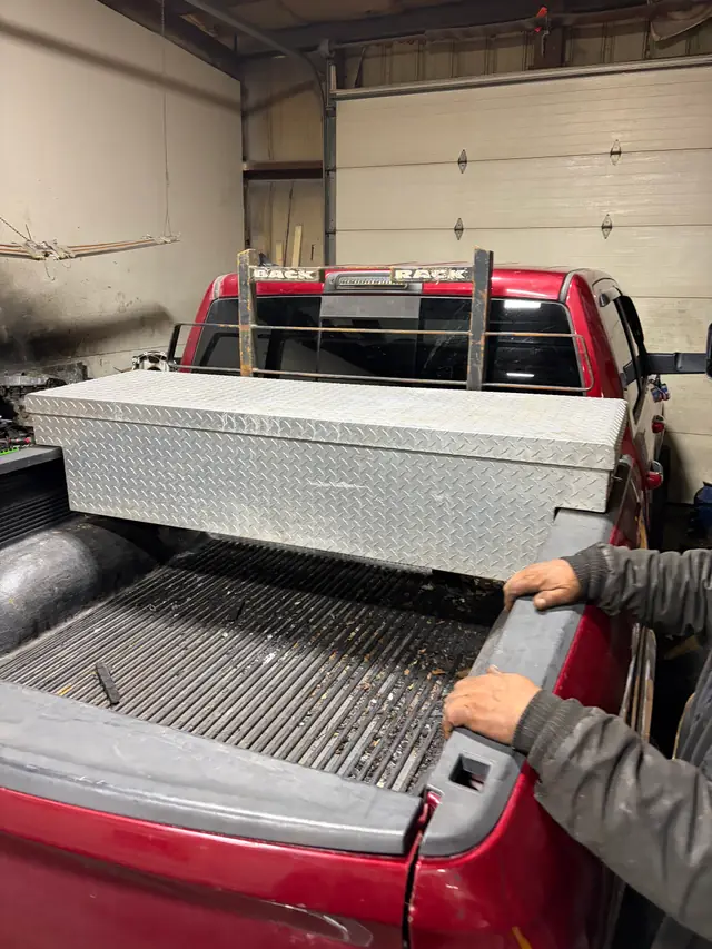 A hand resting on the bed rail of a red pickup fitted with a toolbox