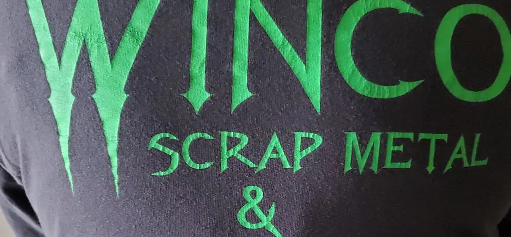 Green WINCO Scrap Metal lettering printed on a charcoal staff shirt