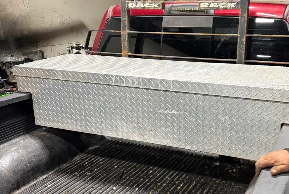 Diamond-plate aluminum truck toolbox set on a red pickup bed under a headache rack